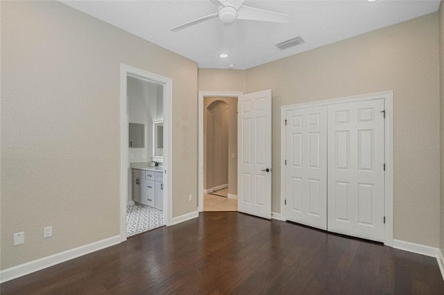 unfurnished bedroom with ensuite bathroom, dark wood-type flooring, ceiling fan, and a closet