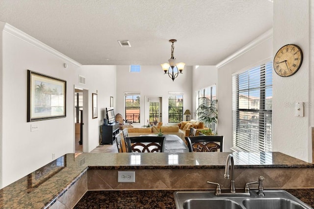 kitchen with crown molding, dark stone counters, a textured ceiling, decorative light fixtures, and sink