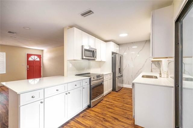 kitchen featuring kitchen peninsula, stainless steel appliances, dark wood-type flooring, sink, and white cabinets