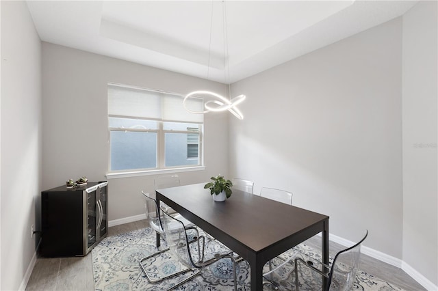 dining area with a notable chandelier, light hardwood / wood-style floors, and a raised ceiling