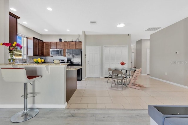 kitchen with appliances with stainless steel finishes, a kitchen bar, light tile patterned floors, kitchen peninsula, and light stone countertops