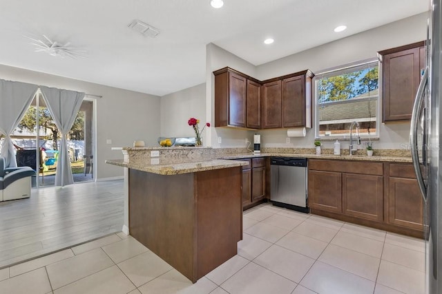 kitchen with sink, light tile patterned floors, appliances with stainless steel finishes, kitchen peninsula, and light stone countertops