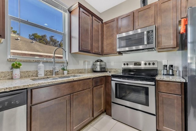 kitchen featuring light tile patterned flooring, stainless steel appliances, light stone countertops, and sink