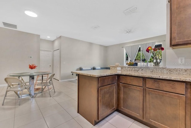 kitchen featuring light stone countertops, kitchen peninsula, and light tile patterned flooring