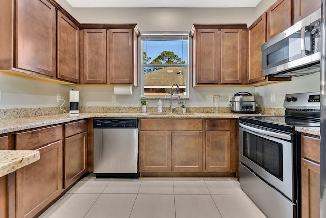 kitchen featuring appliances with stainless steel finishes, sink, light tile patterned floors, and light stone counters