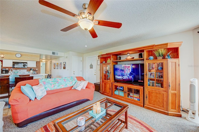 living room with ceiling fan, a textured ceiling, and light carpet