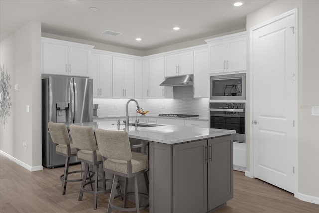 kitchen featuring white cabinets, sink, hardwood / wood-style flooring, an island with sink, and stainless steel appliances