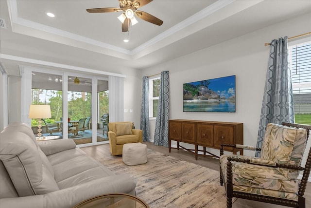 living room with hardwood / wood-style floors, ceiling fan, ornamental molding, and a tray ceiling