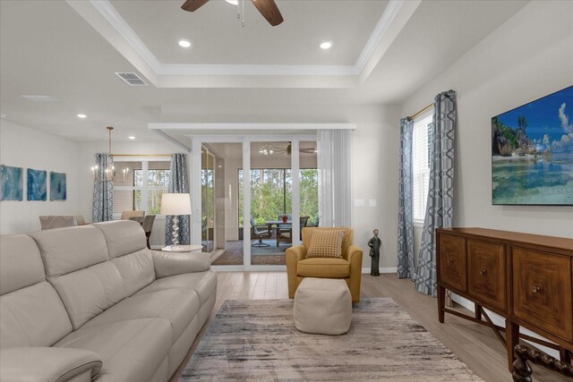 living room featuring ceiling fan with notable chandelier, a raised ceiling, and light hardwood / wood-style flooring