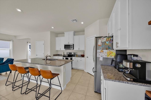 kitchen featuring sink, stainless steel appliances, dark stone countertops, a kitchen island with sink, and white cabinets