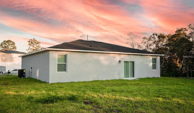 back house at dusk featuring central AC and a yard