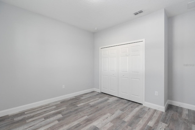 unfurnished bedroom with light hardwood / wood-style floors, a textured ceiling, and a closet