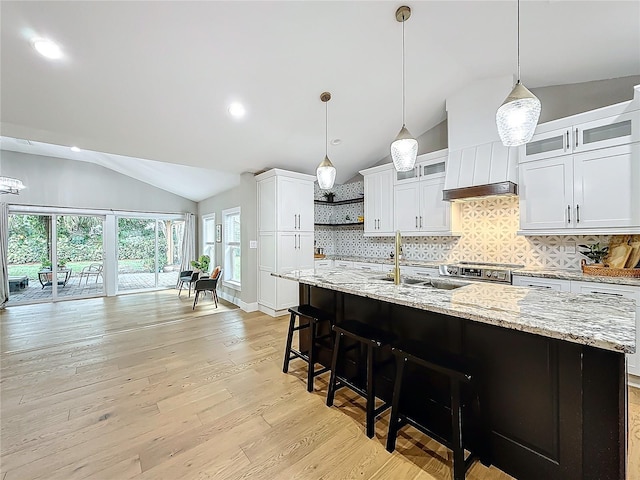 kitchen featuring white cabinets, light wood-type flooring, a center island with sink, and lofted ceiling