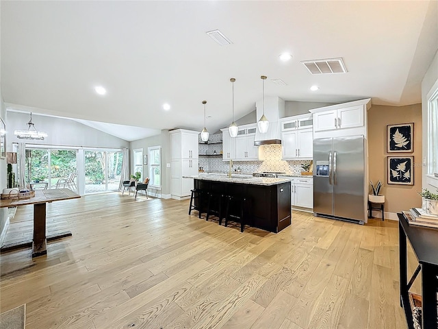 kitchen with hanging light fixtures, a kitchen breakfast bar, built in fridge, light hardwood / wood-style flooring, and a center island with sink