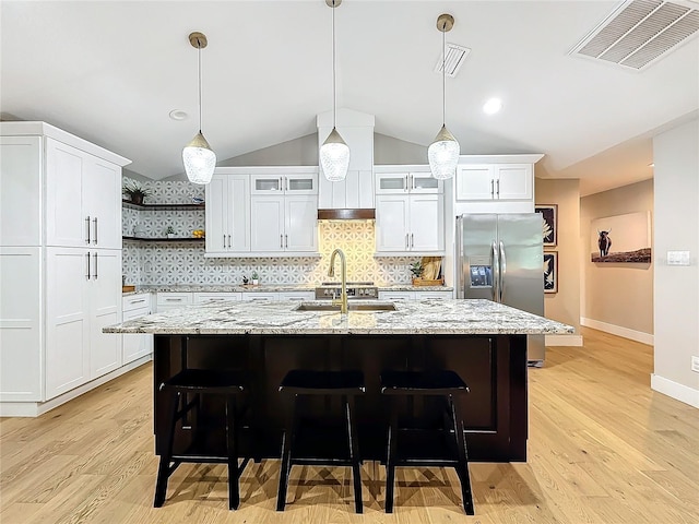 kitchen with stainless steel refrigerator with ice dispenser, light stone counters, sink, a center island with sink, and white cabinetry