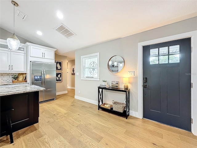 kitchen with stainless steel fridge, light stone counters, white cabinetry, and light wood-type flooring