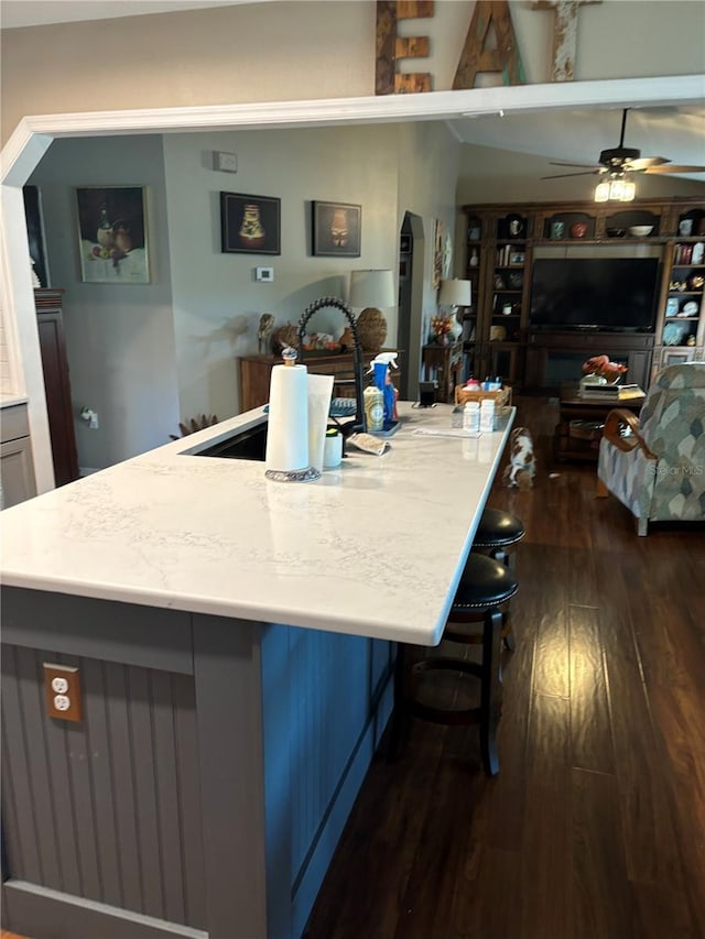 kitchen with a kitchen breakfast bar, dark hardwood / wood-style floors, an island with sink, and ceiling fan