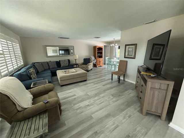 living room with a chandelier, a healthy amount of sunlight, a textured ceiling, and light hardwood / wood-style flooring