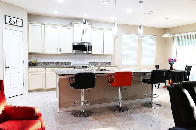 kitchen featuring backsplash, pendant lighting, a kitchen island with sink, light tile patterned floors, and appliances with stainless steel finishes