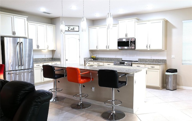 kitchen with a breakfast bar, hanging light fixtures, a kitchen island with sink, light stone countertops, and stainless steel appliances