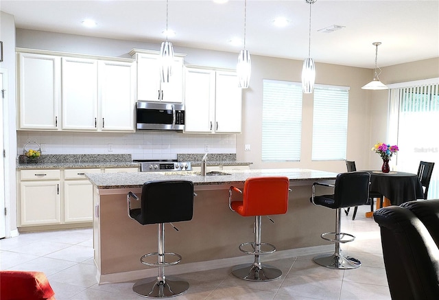 kitchen with a center island with sink, white cabinetry, stainless steel appliances, and pendant lighting