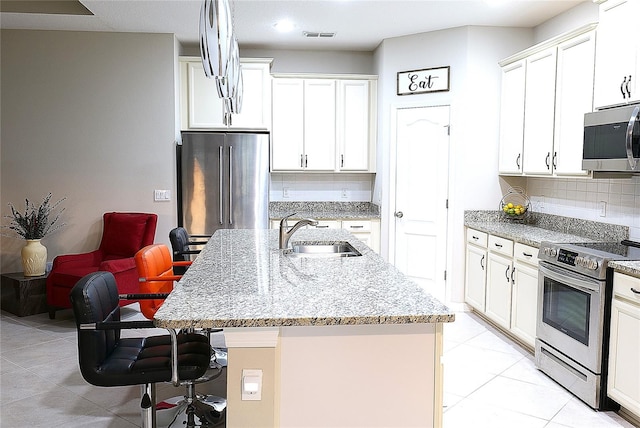 kitchen with sink, backsplash, an island with sink, a breakfast bar area, and appliances with stainless steel finishes