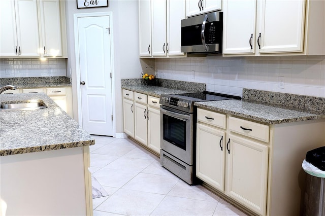 kitchen with light stone countertops, sink, stainless steel appliances, backsplash, and light tile patterned floors