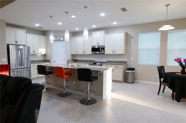 kitchen with a kitchen breakfast bar, light stone counters, decorative light fixtures, a center island with sink, and appliances with stainless steel finishes