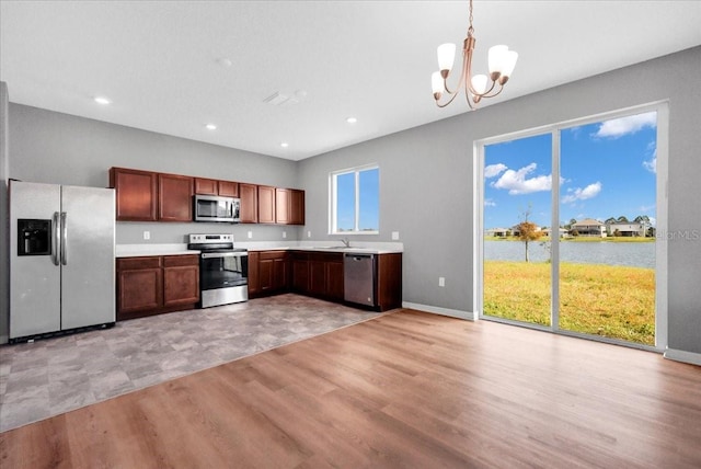 kitchen with a water view, pendant lighting, appliances with stainless steel finishes, an inviting chandelier, and light wood-type flooring