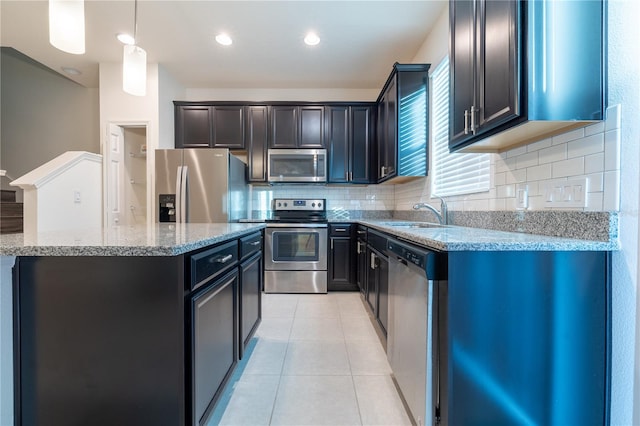 kitchen with light stone counters, stainless steel appliances, sink, decorative light fixtures, and a center island