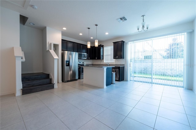 kitchen with backsplash, a chandelier, decorative light fixtures, a kitchen island, and appliances with stainless steel finishes