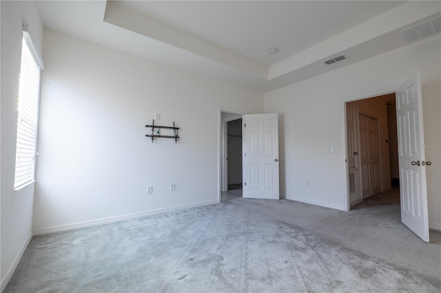 unfurnished bedroom with light carpet and a tray ceiling