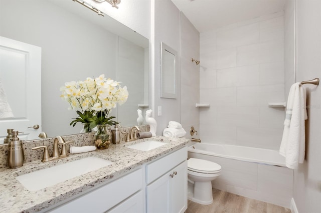 full bath featuring toilet, double vanity, a sink, and wood finished floors