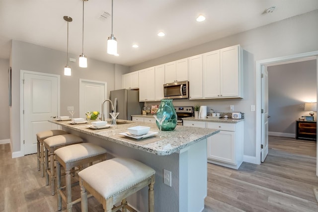 kitchen featuring a center island with sink, light wood-style flooring, a breakfast bar area, stainless steel appliances, and white cabinetry