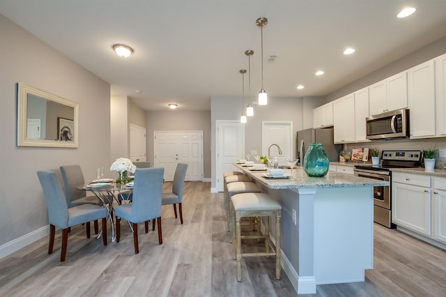 kitchen with light stone counters, appliances with stainless steel finishes, white cabinets, a kitchen island with sink, and light wood-type flooring