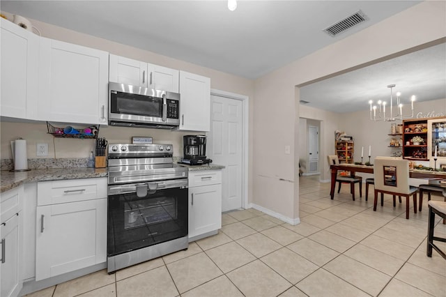 kitchen featuring light tile patterned floors, appliances with stainless steel finishes, a notable chandelier, light stone counters, and white cabinetry