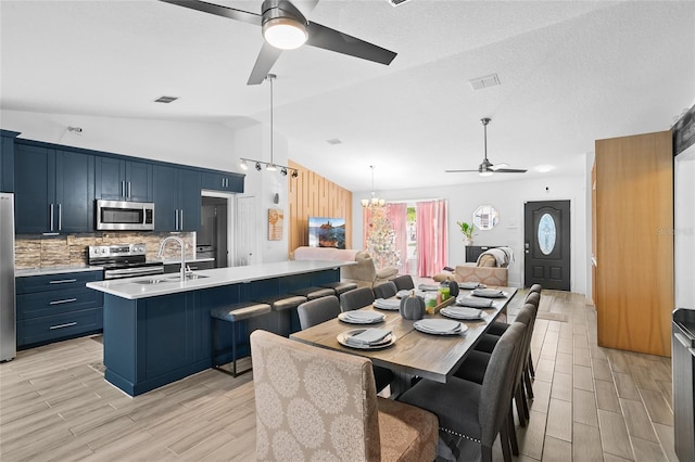 dining area featuring sink, ceiling fan with notable chandelier, lofted ceiling, and light wood-type flooring