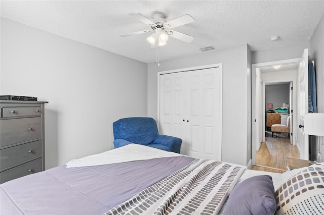 bedroom with ceiling fan, a closet, light hardwood / wood-style floors, and a textured ceiling