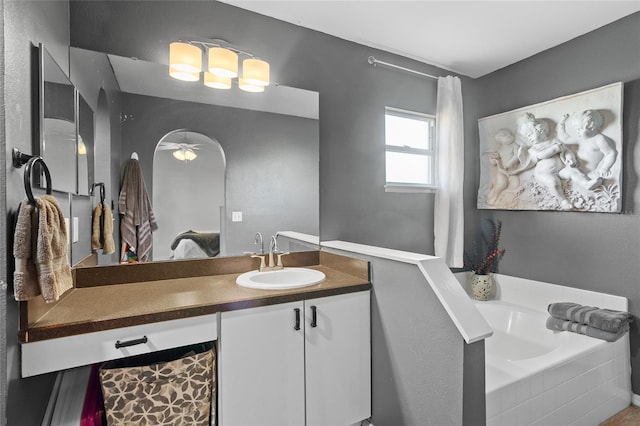 bathroom featuring ceiling fan, vanity, and tiled bath