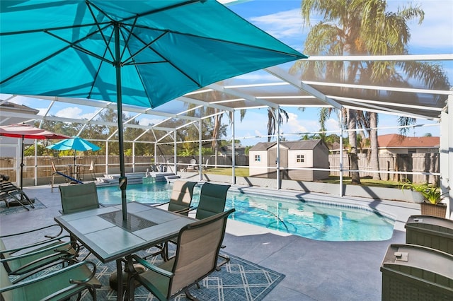 view of swimming pool featuring glass enclosure, a shed, and a patio area