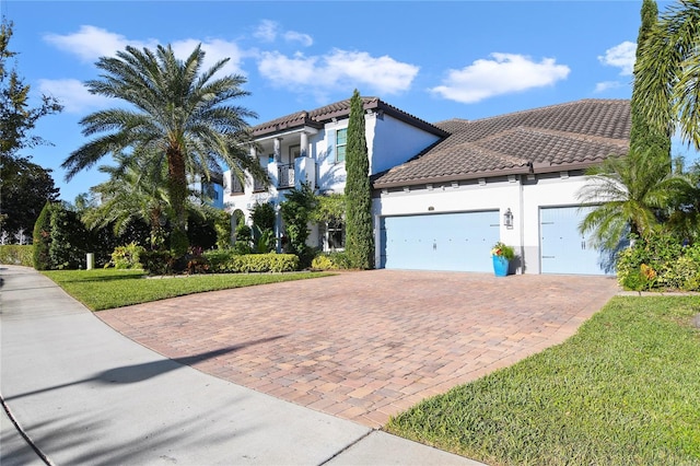 mediterranean / spanish house featuring a garage, stucco siding, a tile roof, decorative driveway, and a front yard