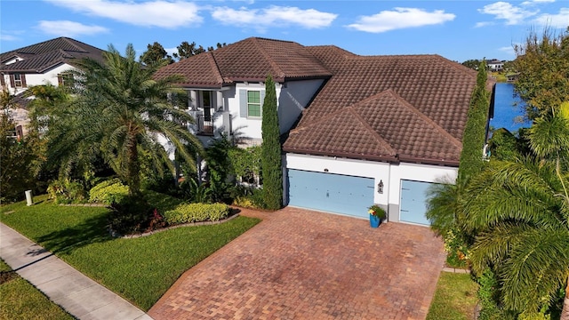 mediterranean / spanish home featuring a garage, decorative driveway, a tiled roof, and stucco siding