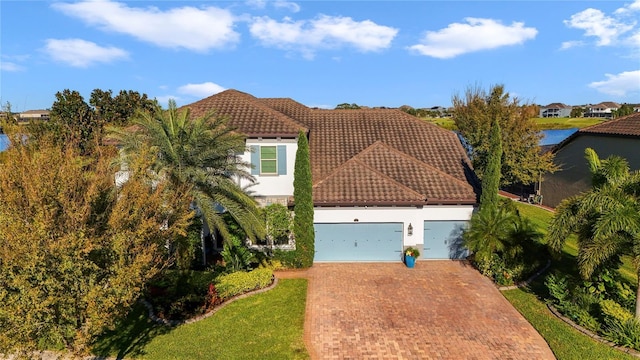 mediterranean / spanish-style home with a garage, decorative driveway, a tile roof, and stucco siding