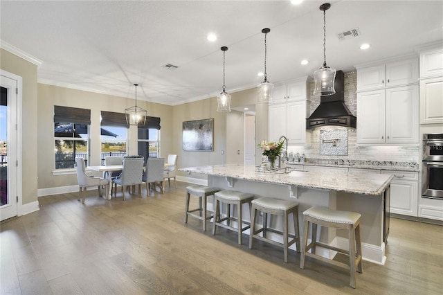 kitchen featuring premium range hood, visible vents, light wood-style flooring, and backsplash