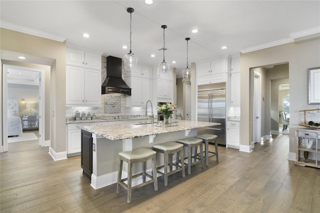 kitchen with premium range hood, built in refrigerator, a sink, white cabinetry, and crown molding