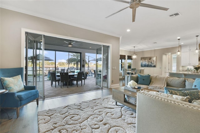 living area featuring plenty of natural light, visible vents, crown molding, and wood finished floors