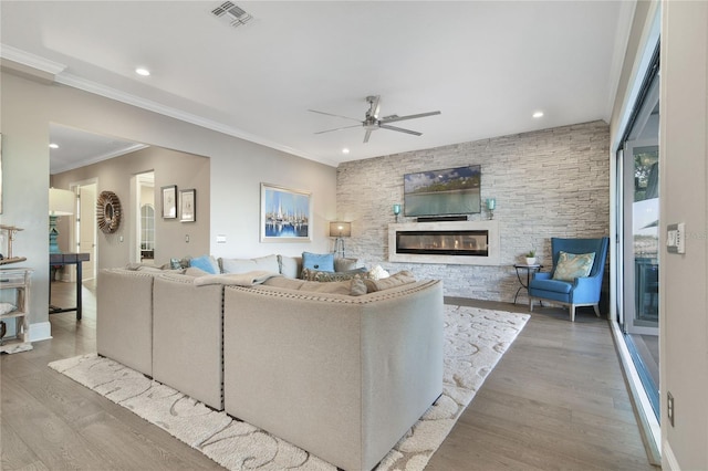 living room featuring a large fireplace, visible vents, ceiling fan, ornamental molding, and wood finished floors