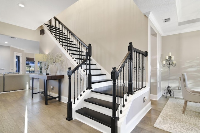 staircase with ornamental molding, wood finished floors, visible vents, and baseboards