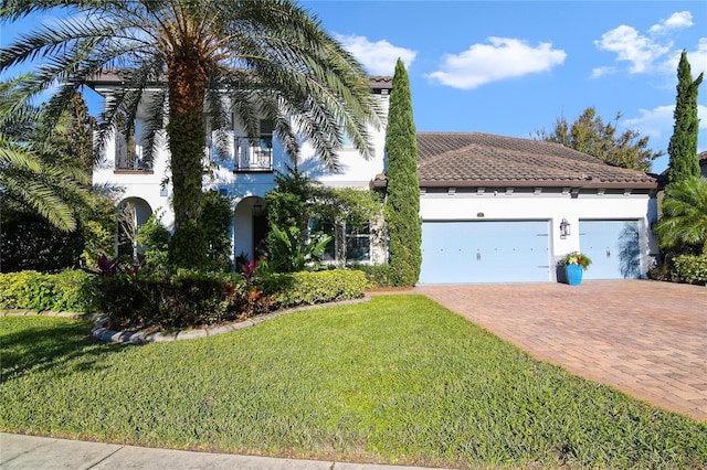 mediterranean / spanish-style house with decorative driveway, stucco siding, a balcony, a garage, and a front lawn