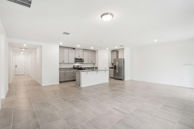 kitchen featuring gray cabinetry, light tile patterned floors, an island with sink, light stone counters, and stainless steel appliances